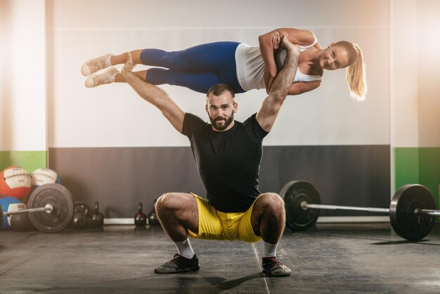 Young muscular man doing squats exercise and holding girl above.