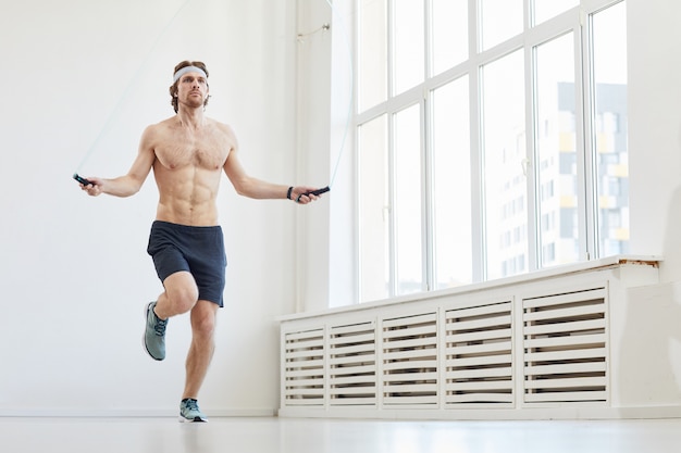 Young muscular man jumping on skipping rope during sports training