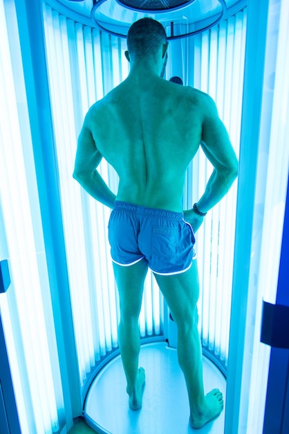 Young muscular man at solarium in beauty salon