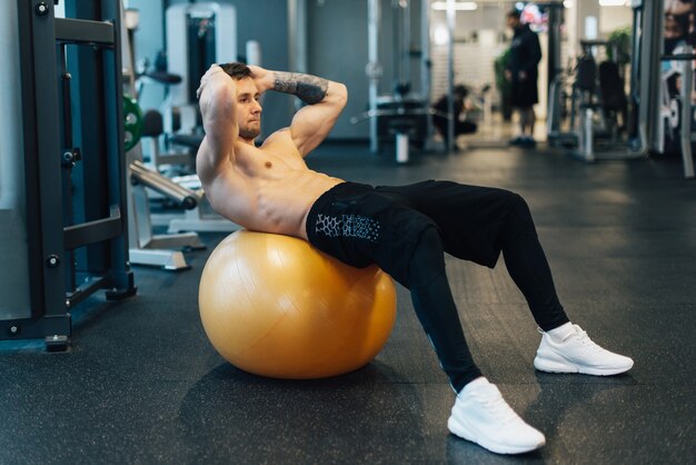 Young muscular man trains abdominal muscles using exercise ball