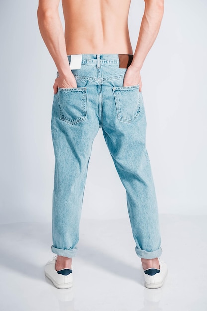 Young muscular man with a naked torso dressed in blue jeans on\
a white background