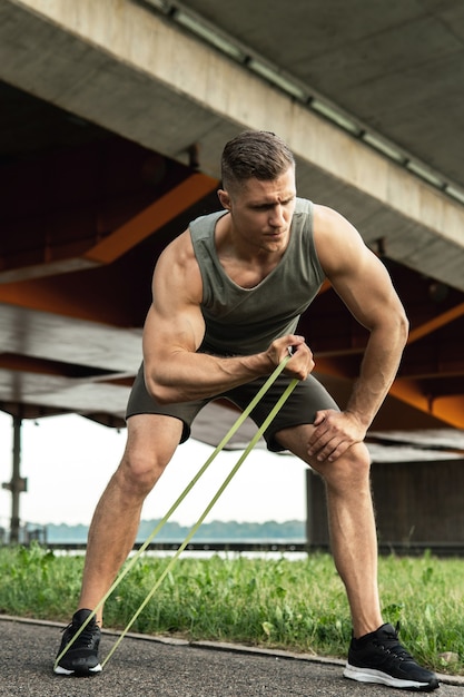 Young and muscular man during workout with a resistance rubber bands on a street. Biceps curls exercise.