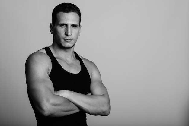 young muscular Persian man with arms crossed against gray wall