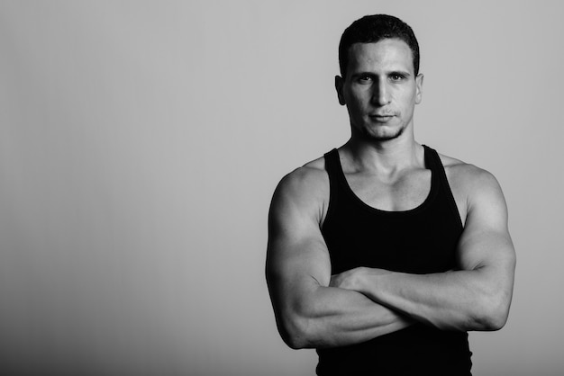 young muscular Persian man  with arms crossed against gray wall