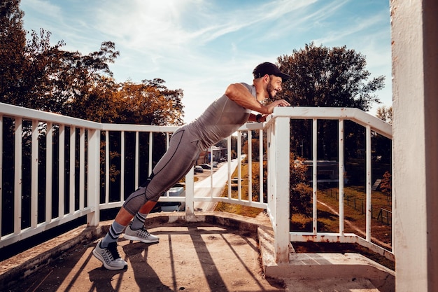 Молодой мускулистый спортсмен отжимается на мосту.