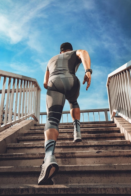 Young muscular sportsman running up the stairs at the bridge. Rear view.