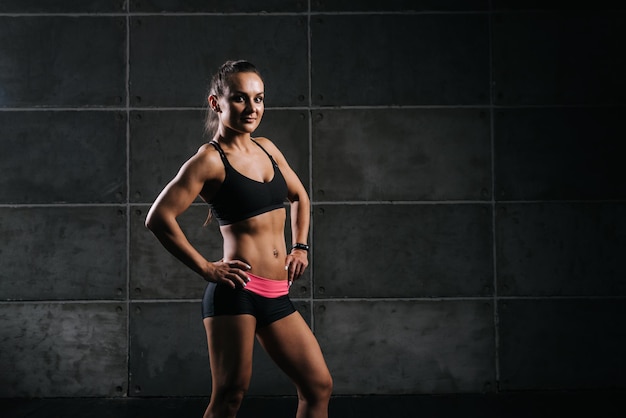 Young muscular woman bodybuilder is standing with hands on her belt