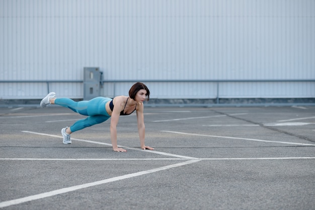 Young muscular woman doing core exercise. Fit female doing press-ups during the training outdoors.