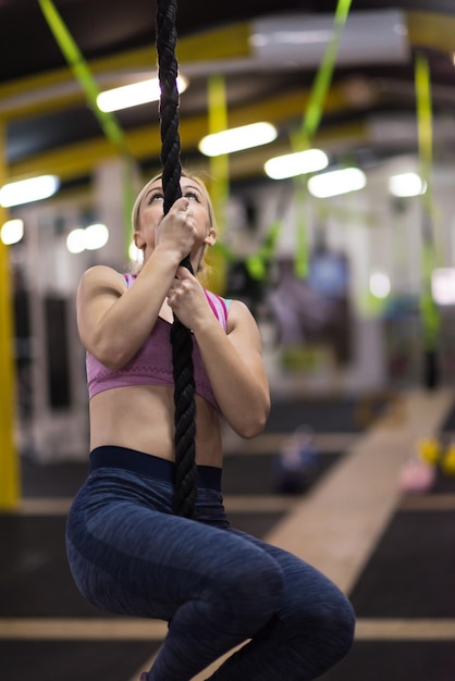 Photo young muscular woman doing rope climbing in cross fitness gym