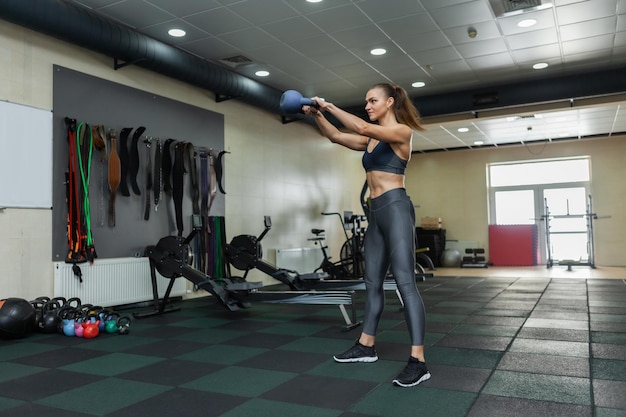 Young muscular woman in sportswear trains kettlebell swing in the gym. Healthy lifestyle concept. Functional training