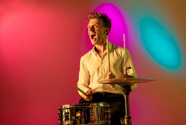 Young musician, drummer in neon in studio