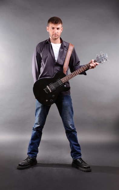 Young musician playing guitar on gray background