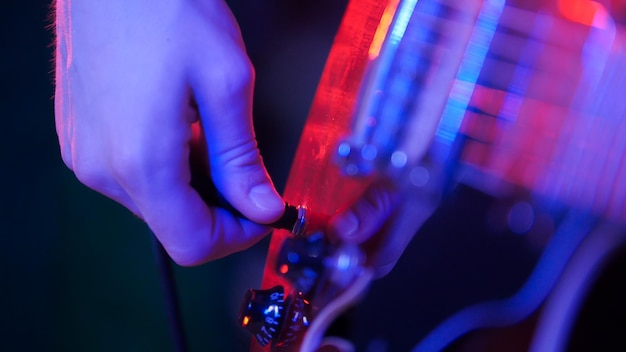 Young musician playing guitar in neon lighting Plugging in the plug