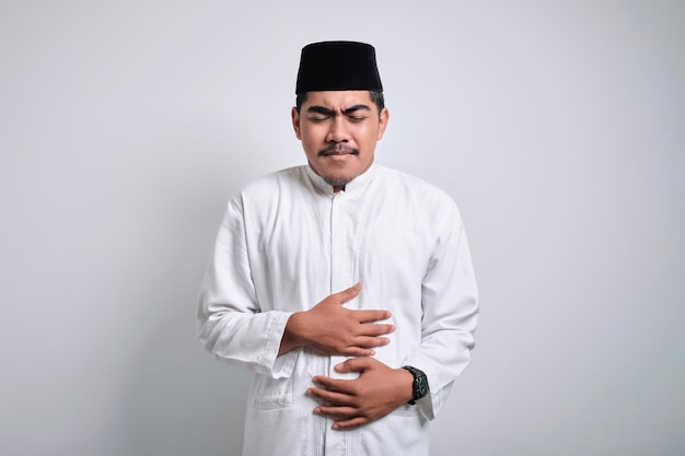 Young muslim Asian man in white clothes squezze his stomach for having stomachache pain