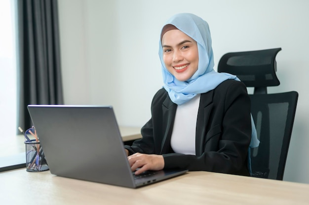 Photo young muslim business woman working on laptop with documents in modern office