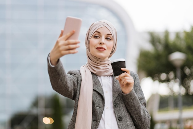 Young Muslim businesslady economist in formal wear holding a cup of coffee