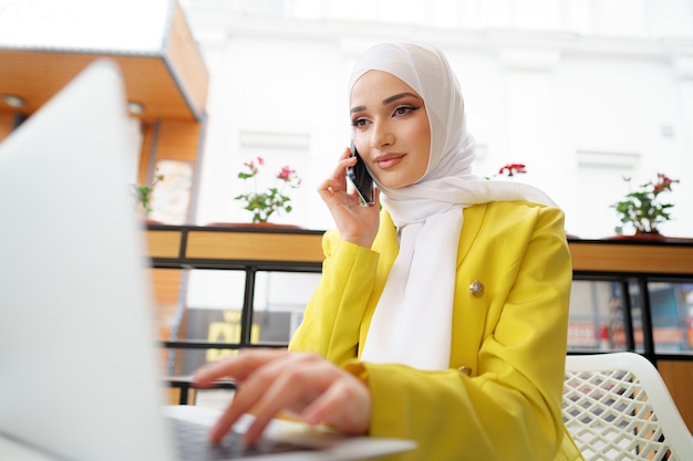 Young muslim businesswoman in headscarf sitting in cafe and talking on the phone