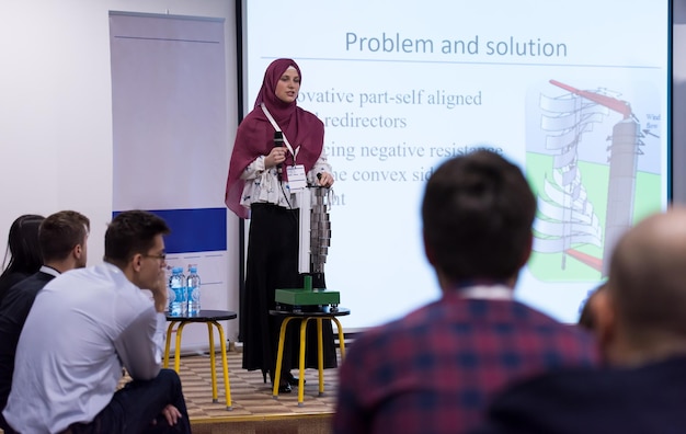 молодая мусульманская деловая женщина с красным шарфом в бизнес-конференц-зале, выступая с публичными презентациями. Аудитория в конференц-зале. Клуб предпринимательства