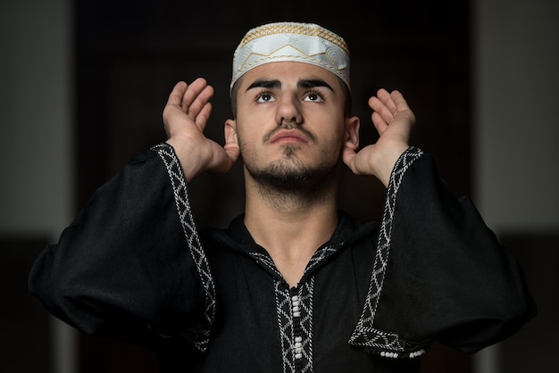 Young Muslim Guy Making Traditional Prayer To God While Wearing A Traditional Cap Dishdasha