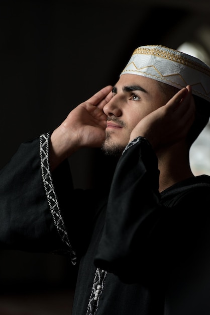 Young Muslim Guy Making Traditional Prayer To God While Wearing A Traditional Cap Dishdasha