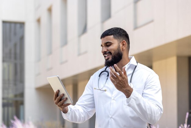 Photo a young muslim male doctor stands near the hospital on the street in a white coat and talks on the