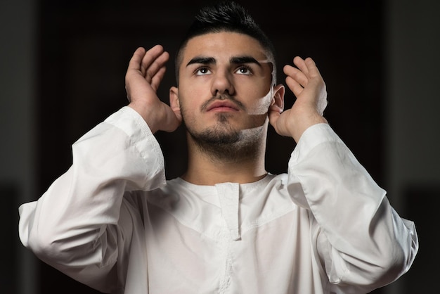 Young Muslim Man Making Traditional Prayer To God While Wearing A Traditional Cap Dishdasha