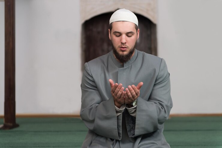 Photo young muslim man making traditional prayer to god while wearing a traditional cap dishdasha