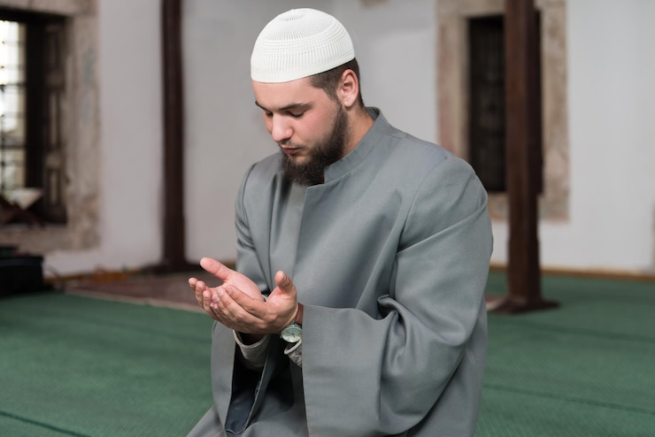 Photo young muslim man making traditional prayer to god while wearing a traditional cap dishdasha