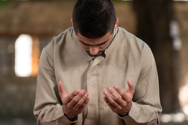 Photo young muslim man making traditional prayer to god while wearing a traditional cap dishdasha