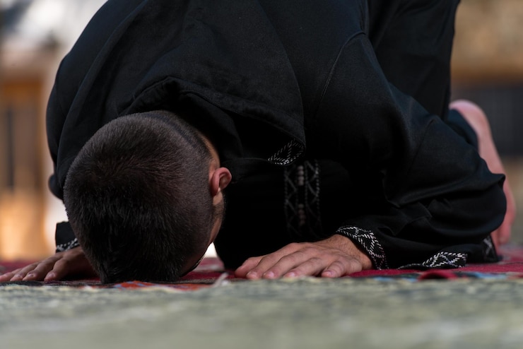 Photo young muslim man making traditional prayer to god while wearing a traditional cap dishdasha