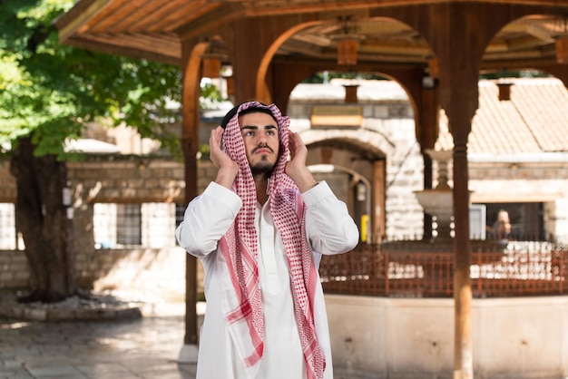 Young Muslim Man Making Traditional Prayer To God While Wearing A Traditional Cap Dishdasha