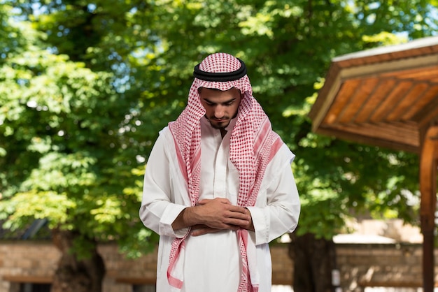 伝統的な帽子のディシュダシャを身に着けている間、神に伝統的な祈りをする若いイスラム教徒の男