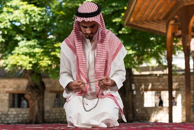 Young Muslim Man Making Traditional Prayer To God While Wearing A Traditional Cap Dishdasha