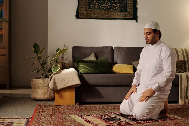 Молодой мусульманский мужчина молится в гостиной