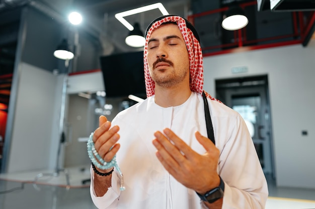 Young muslim man with rosary beads praying in the office