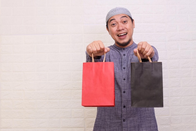흰색 배경에 격리된 쇼핑백을 들고 웃고 있는 젊은 이슬람 쇼핑 중독자