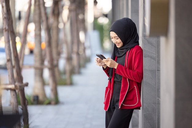 通りに立っている携帯電話を保持して成功を祝う若いイスラム教徒の女性