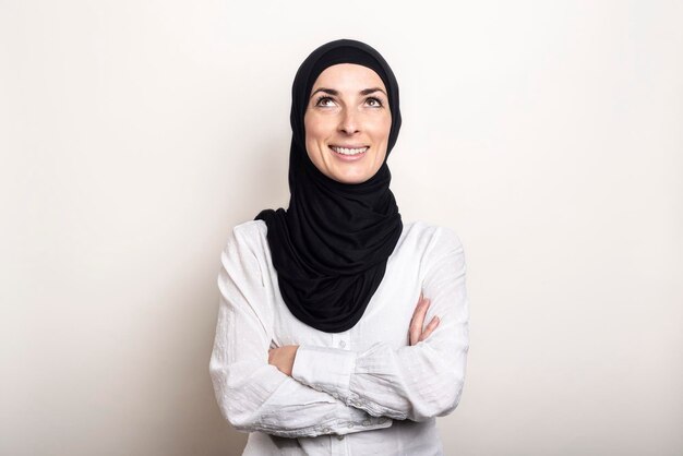 Young Muslim woman dressed in a white shirt and hijab looks up on a light background Banner