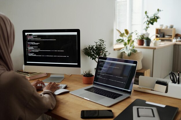 Young Muslim woman in headscarf decoding data or developing new software while typing