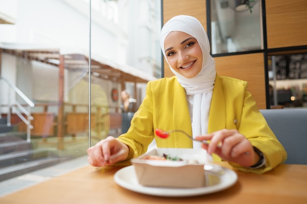 Young muslim woman in hijab having a lunch in cafe