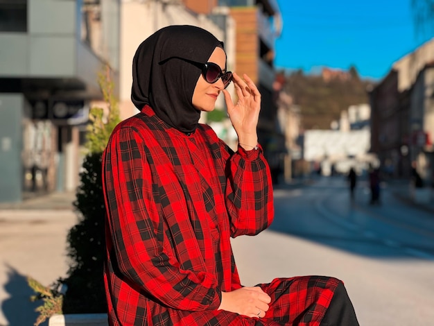 A young Muslim woman in a hijab is sitting on a bench in the city