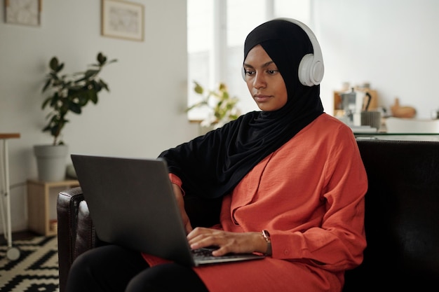 Young Muslim woman in hijab and red shirt typing on laptop keyboard