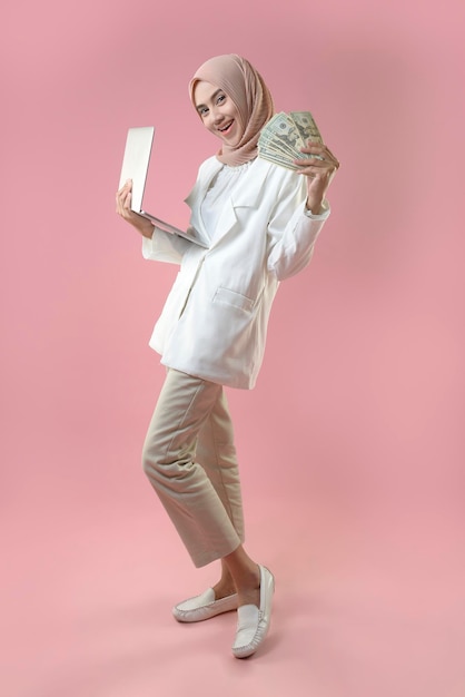 Young muslim woman hold money and laptop on isolated background