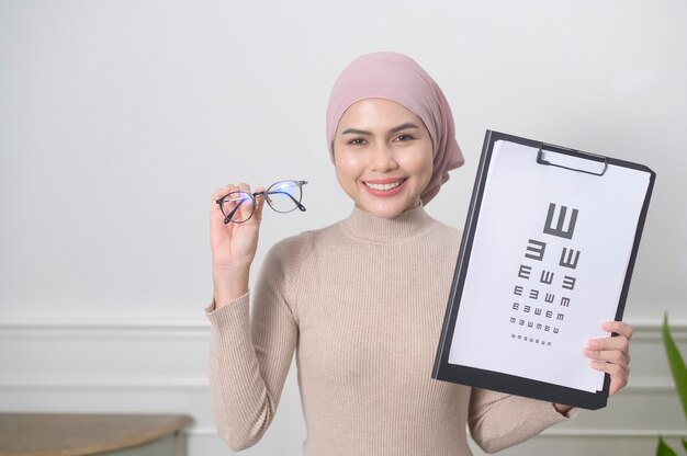Молодая мусульманка держит тест на диаграмму зрения для измерения остроты зрения