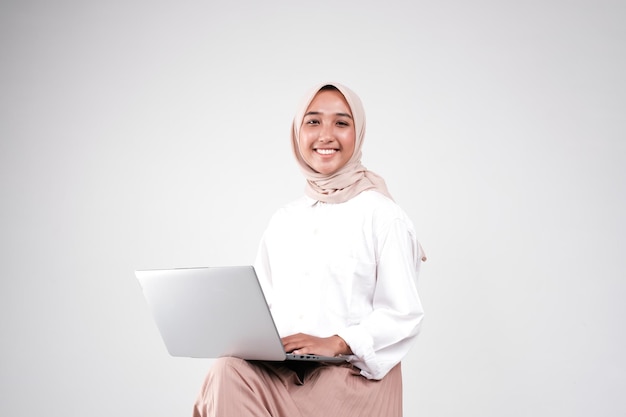 Photo a young muslim woman is sitting on a chair and is holding a laptop