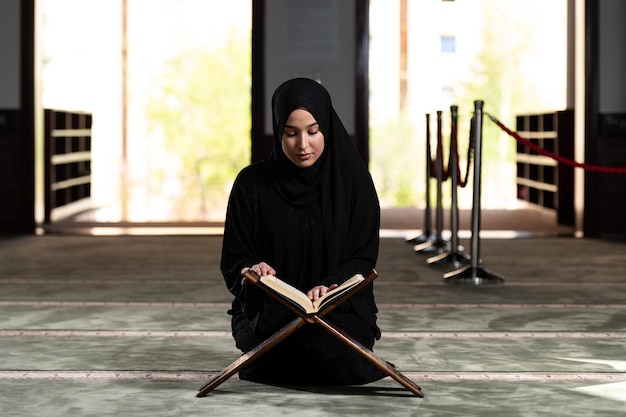 Молодая мусульманка молится в мечети с Кораном