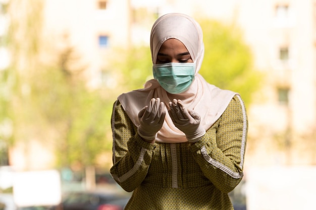 Молодая мусульманка молится в мечети с хирургической маской и перчатками