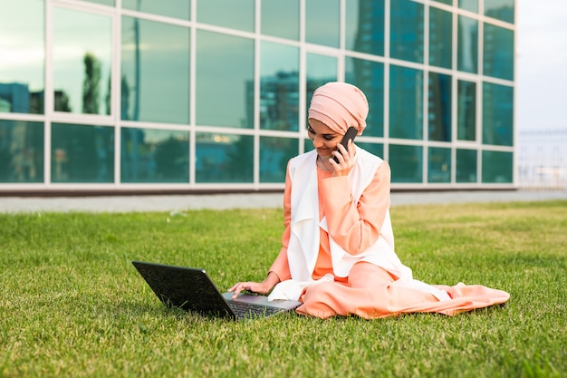 Young muslim woman using mobile phone and laptop in park