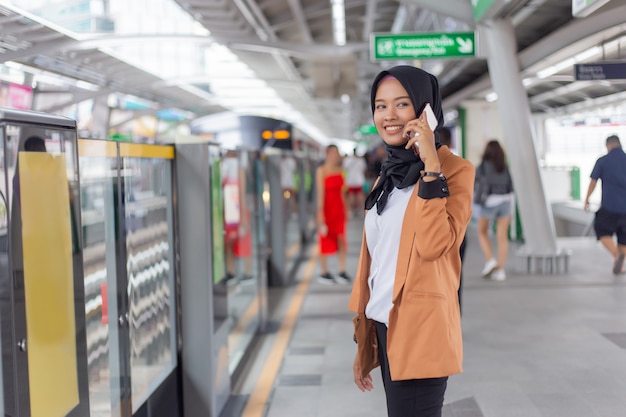 Молодая мусульманская женщина используя телефон на станции skytrain.