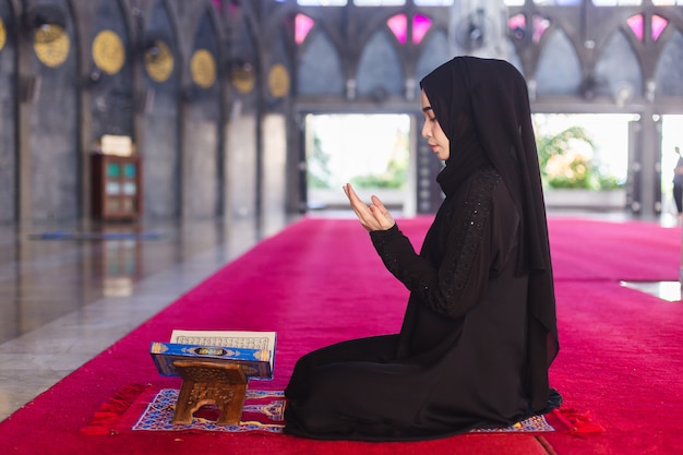 Young muslim woman in wear black dress read quran and making wish praying in mosque. make a wish and read quran in ramadan.